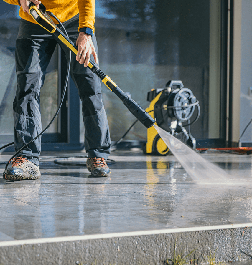 Person using pressure washer on patio.
