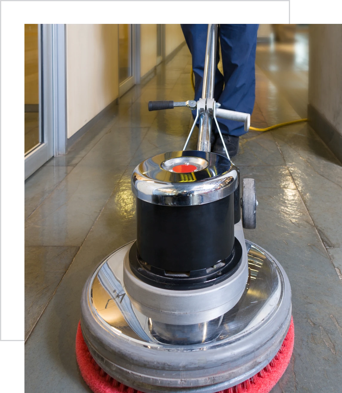 Floor buffer cleaning hallway with red pad.